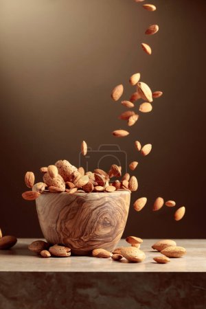 Photo for Almond nuts are poured into a wooden bowl. Brown background with copy space. - Royalty Free Image