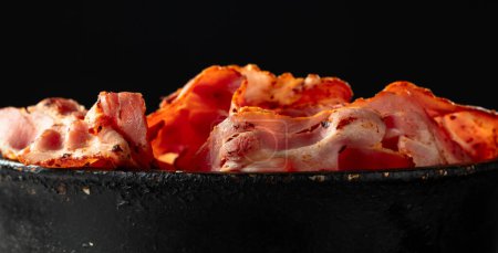 Photo for Fried bacon slices in old black pan on a black background. Copy space. - Royalty Free Image
