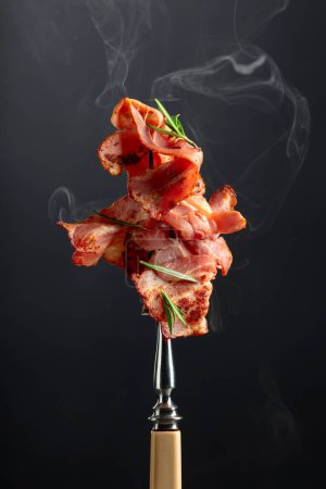 Photo for Hot fried bacon slices with rosemary on a fork. Copy space. - Royalty Free Image