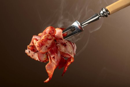 Photo for Roasted bacon slices on a brown background. Roasted bacon on a fork. - Royalty Free Image