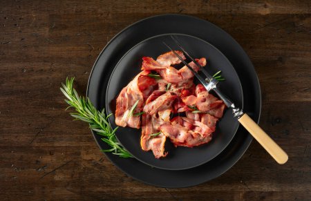 Photo for Roasted bacon slices with rosemary on an  old wooden table. Copy space. Top view. - Royalty Free Image