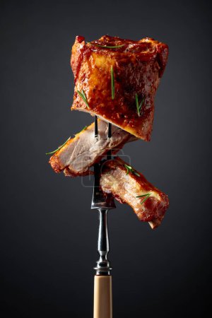 Photo for Grilled pork ribs on a fork. Grilled meat sprinkled with rosemary on a black background. - Royalty Free Image