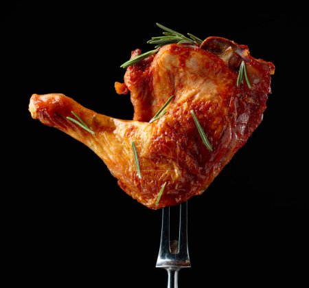 Téléchargez les photos : Jambe de poulet grillée saupoudrée de romarin sur fond noir. Tambour de poulet sur une fourchette. - en image libre de droit