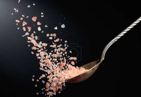 Photo for Pink Himalayan salt is poured with a spoon. Himalaya salt on a dark background. Copy space. - Royalty Free Image