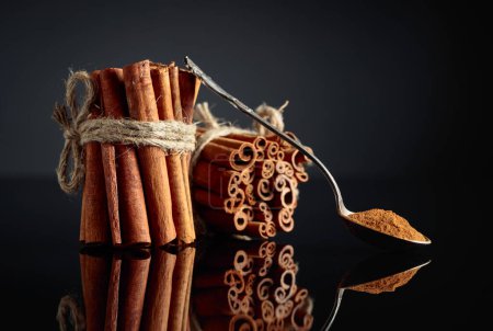 Photo for Ground cinnamon, cinnamon sticks, tied with jute rope on a black reflective background. Copy space. - Royalty Free Image
