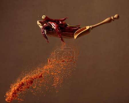 Photo for Pepper powder is poured out of the wooden spoon. Wooden dish with dried chili pepper and a spoon with ground pepper. - Royalty Free Image