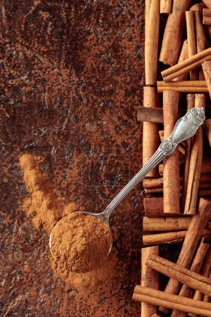 Photo for Cinnamon powder in a spoon and cinnamon sticks on a brown background. Top view. Copy space. - Royalty Free Image