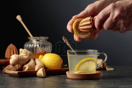 Foto de Té de jengibre con limón y miel sobre fondo negro. El jugo se exprime de un limón con un exprimidor de madera viejo. - Imagen libre de derechos