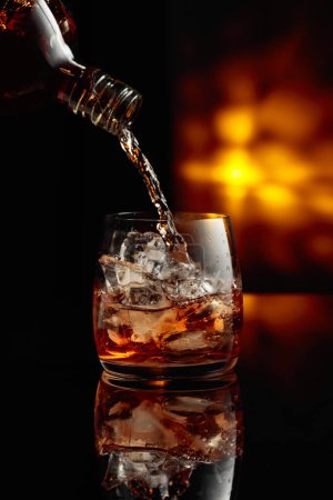 Photo for Pouring whiskey from a bottle into a glass with ice. - Royalty Free Image