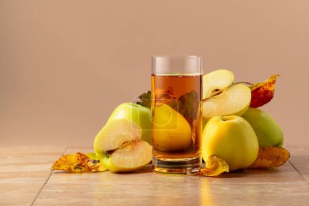 Téléchargez les photos : Jus de pomme et pommes mûres aux feuilles séchées. Fond beige avec espace de copie. - en image libre de droit