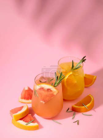 Foto de Cócteles de verano con pomelo, naranja, romero y hielo. Bebidas sobre fondo rosa con sombra de hoja de palma. Copiar espacio. - Imagen libre de derechos