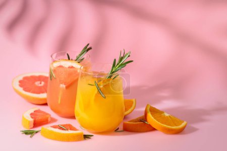 Foto de Cócteles de verano con pomelo, naranja, romero y hielo. Bebidas sobre fondo rosa con sombra de hoja de palma. Copiar espacio. - Imagen libre de derechos
