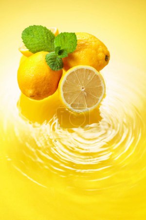 Photo for Ripe juicy lemons with mint on a yellow background with water splashes. Copy space. - Royalty Free Image
