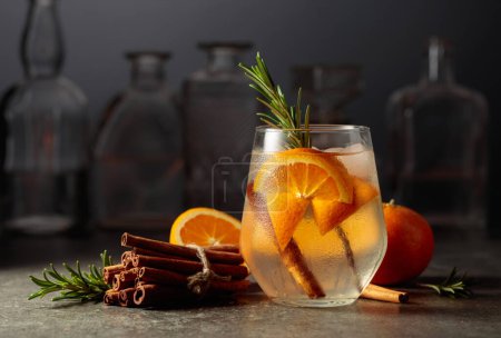 Téléchargez les photos : Cocktail gin tonic avec glace, romarin, cannelle et orange sur une table en pierre dans un bar. - en image libre de droit