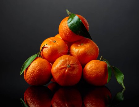 Téléchargez les photos : Tangerines aux feuilles vertes sur fond noir réfléchissant. - en image libre de droit