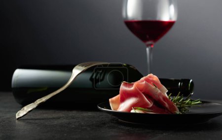 Téléchargez les photos : Prosciutto au romarin et vin rouge sur fond noir. Copiez l'espace pour votre texte. - en image libre de droit