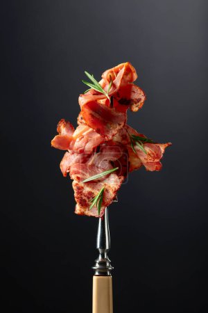 Téléchargez les photos : Tranches de bacon frites chaudes avec romarin sur une fourchette. Espace de copie. - en image libre de droit