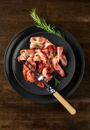 Téléchargez les photos : Tranches de bacon rôties avec romarin sur une vieille table en bois. Espace de copie. Vue du dessus. - en image libre de droit