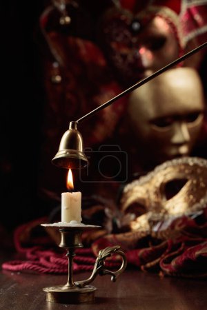 Photo for Burning candle in an old brass candlestick and carnival masks on an old wooden table. - Royalty Free Image