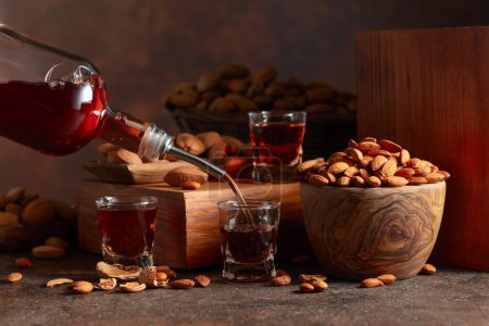 Photo for Italian liqueur Amaretto with almonds nuts on a vintage table. Liqueur is poured from a bottle into a glass. - Royalty Free Image