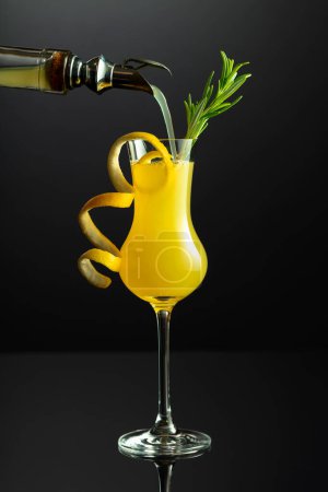 Téléchargez les photos : Liqueur italienne traditionnelle Limoncello avec brindille de romarin sur fond réfléchissant noir. L'alcool est versé d'une bouteille dans un verre. - en image libre de droit