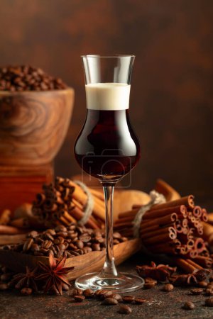 Foto de Licor de café con crema sobre fondo marrón. Los granos de café, los palitos de canela y el anís están esparcidos en la mesa. - Imagen libre de derechos