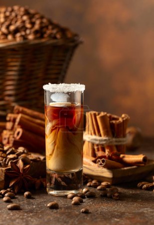 Téléchargez les photos : Liqueur de café avec crème sur fond brun. Des grains de café, des bâtonnets de cannelle et de l'anis sont éparpillés sur la table. - en image libre de droit