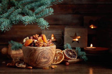 Foto de Frutas secas y frutos secos surtidos en una mesa de madera vieja. Bodegón de Navidad con ramas de abeto y velas encendidas en linternas viejas. - Imagen libre de derechos