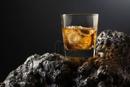 Téléchargez les photos : Whisky avec glace sur une pierre grise. Fond noir avec espace de copie. - en image libre de droit