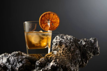 Téléchargez les photos : Cocktail à l'ancienne avec glace et tranche d'orange séchée sur une pierre grise. Fond noir avec espace de copie. - en image libre de droit