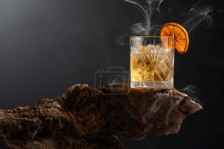 Photo for Smoked old fashioned rum cocktail with ice and dried orange slice on a old wooden snag. Copy space. - Royalty Free Image