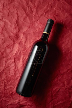 Photo for Bottle of red wine on a crumpled red paper background. Top view. - Royalty Free Image