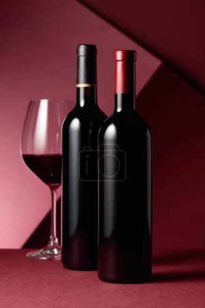 Téléchargez les photos : Verre et bouteilles de vin rouge sur fond rouge. Espace de copie. - en image libre de droit
