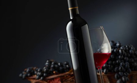 Photo for Bottle and glass of red wine with blue grapes. Black background with copy space. Focus on a foreground. - Royalty Free Image