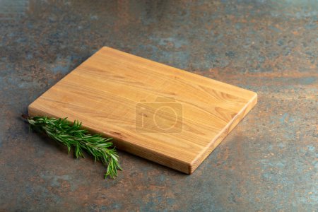 Photo for Cutting board and rosemary on a rusty iron table. Culinary background. Empty wooden cutting board, product display space. - Royalty Free Image