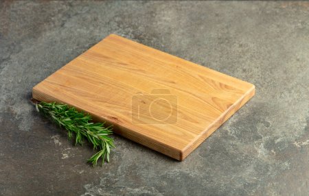 Photo for Cutting board and rosemary on a stone table. Culinary background. Empty wooden cutting board, product display space. - Royalty Free Image