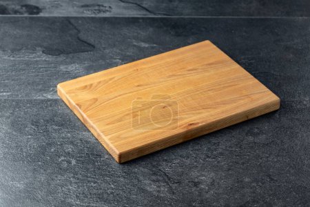 Téléchargez les photos : Planche à découper sur une table en pierre noire. Fond culinaire. Planche à découper en bois vide, espace d'affichage des produits. - en image libre de droit