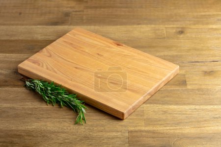 Photo for Cutting board and rosemary on an old wooden table. Culinary background. Empty wooden cutting board, product display space. - Royalty Free Image