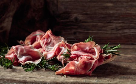 Photo for Italian prosciutto crudo or Spanish jamon with rosemary on an old wooden background. Copy space. - Royalty Free Image