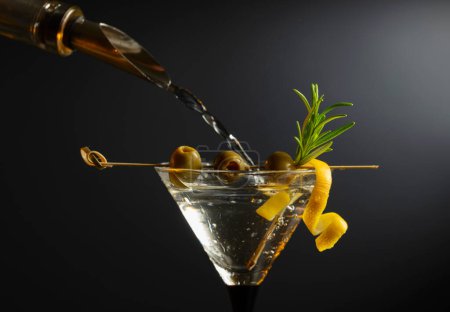 Foto de Cóctel clásico de martini seco con aceitunas verdes, cáscara de limón y romero sobre un fondo negro. Espacio libre para tu texto. - Imagen libre de derechos