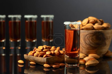 Photo for Strong alcoholic Italian liqueur Amaretto with almonds nuts on a black background. - Royalty Free Image