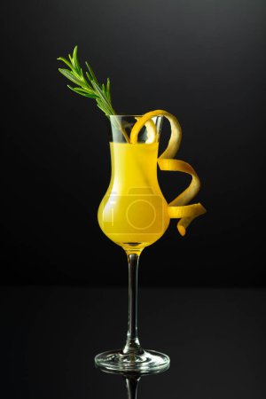 Téléchargez les photos : Liqueur italienne traditionnelle Limoncello avec brindille de romarin sur fond noir réfléchissant. - en image libre de droit
