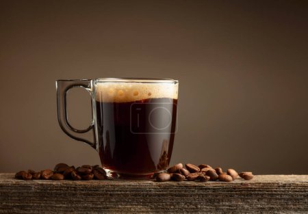 Photo for Espresso coffee glass cup on a brown background. Coffee cup and roasted coffee beans on a old wooden board. Copy space. - Royalty Free Image