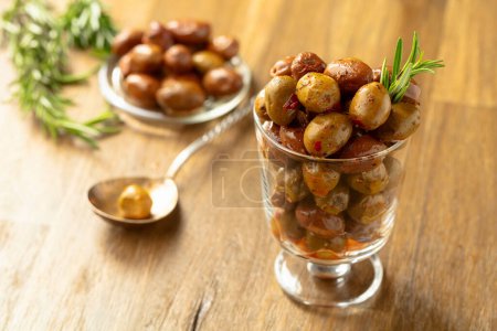 Téléchargez les photos : Olives épicées dans un bol en verre. Bol avec olives conservées et brindilles de romarin sur une table en bois. - en image libre de droit