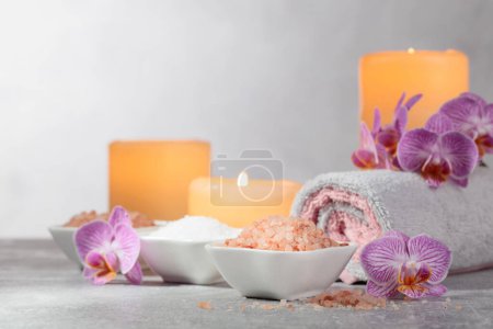 Photo for Sea salt, towels, orchid flowers, and burning candles on a grey background. Spa concept with copy space. - Royalty Free Image