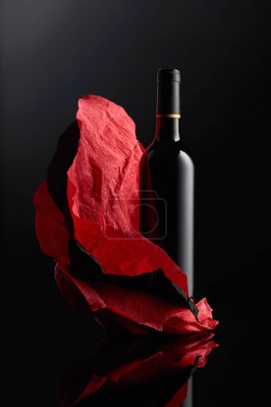 Téléchargez les photos : Bottle of red wine on a crumpled paper. Black reflective background. - en image libre de droit