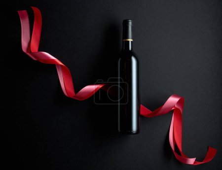 Téléchargez les photos : Bottle of red wine with red and pink satin ribbons. Top view. Copy space. - en image libre de droit