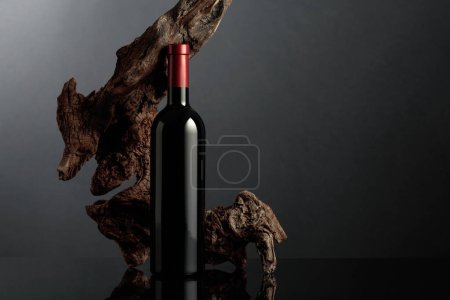 Photo for Bottle of red wine on a black reflective background. In the background old weathered snag. Frontal view with space for your text. - Royalty Free Image