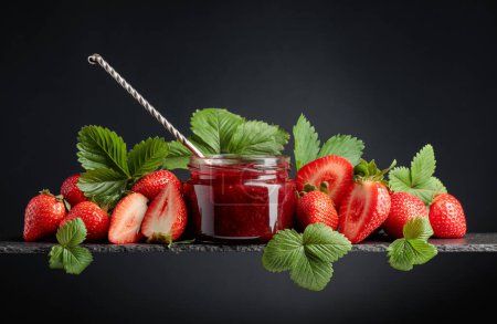 Photo for Strawberry jam in a small jar and fresh berries with leaves on a black background. - Royalty Free Image