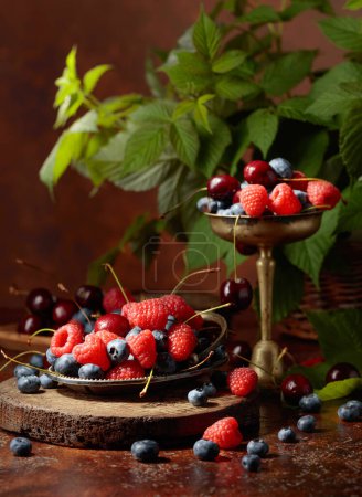 Foto de Bayas con hojas sobre una vieja mesa marrón. Colorida mezcla variada de arándanos, frambuesas y cerezas dulces. - Imagen libre de derechos